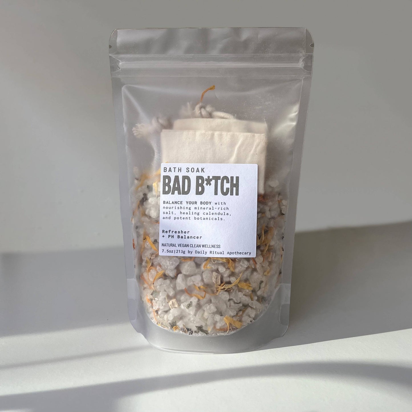 A pouch labeled 'BATH SMOKE BAD B*TCH' filled with dried botanicals and sea salt for bath making.