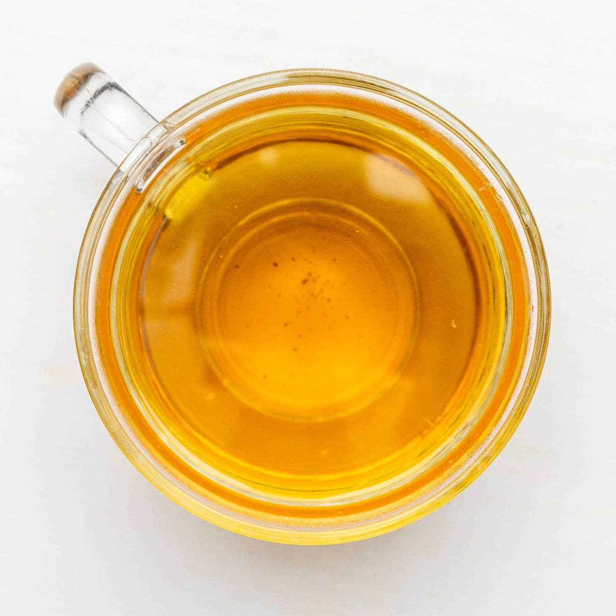 Clear glass mug filled with yellow tea on a white background