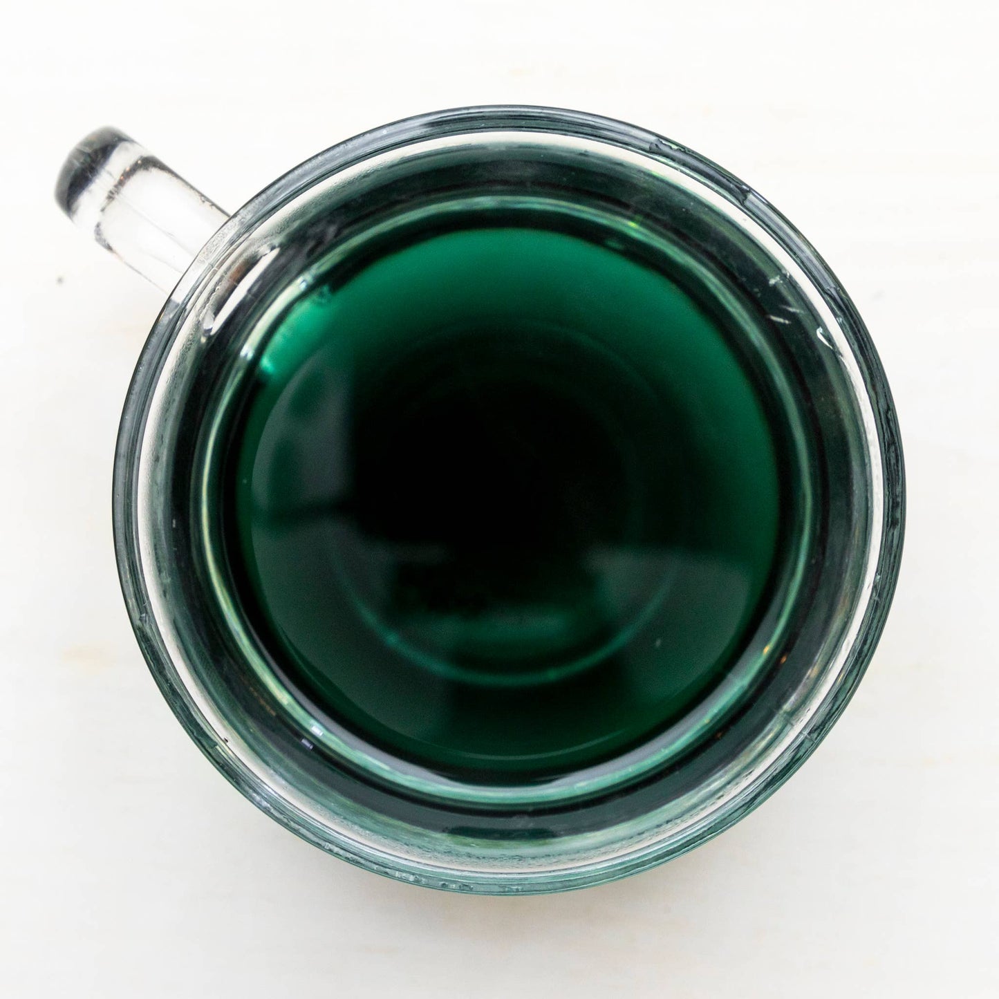 Clear glass mug filled with dark green tea on a white background