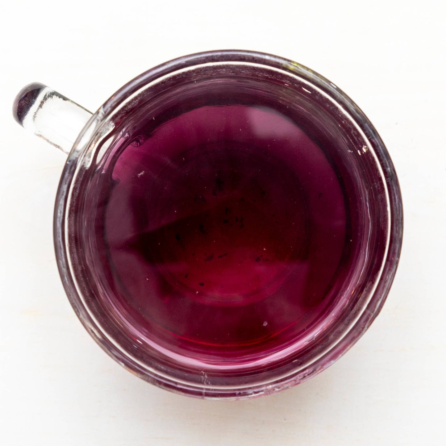 Clear glass mug filled with purple tea on a white background