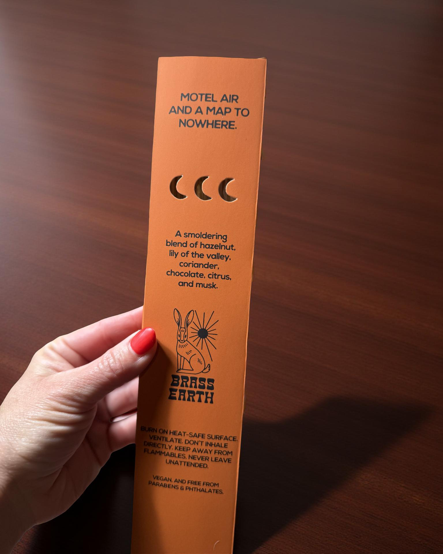 Brass Earth Orange product packaging with text and branding held by a hand on a wooden surface