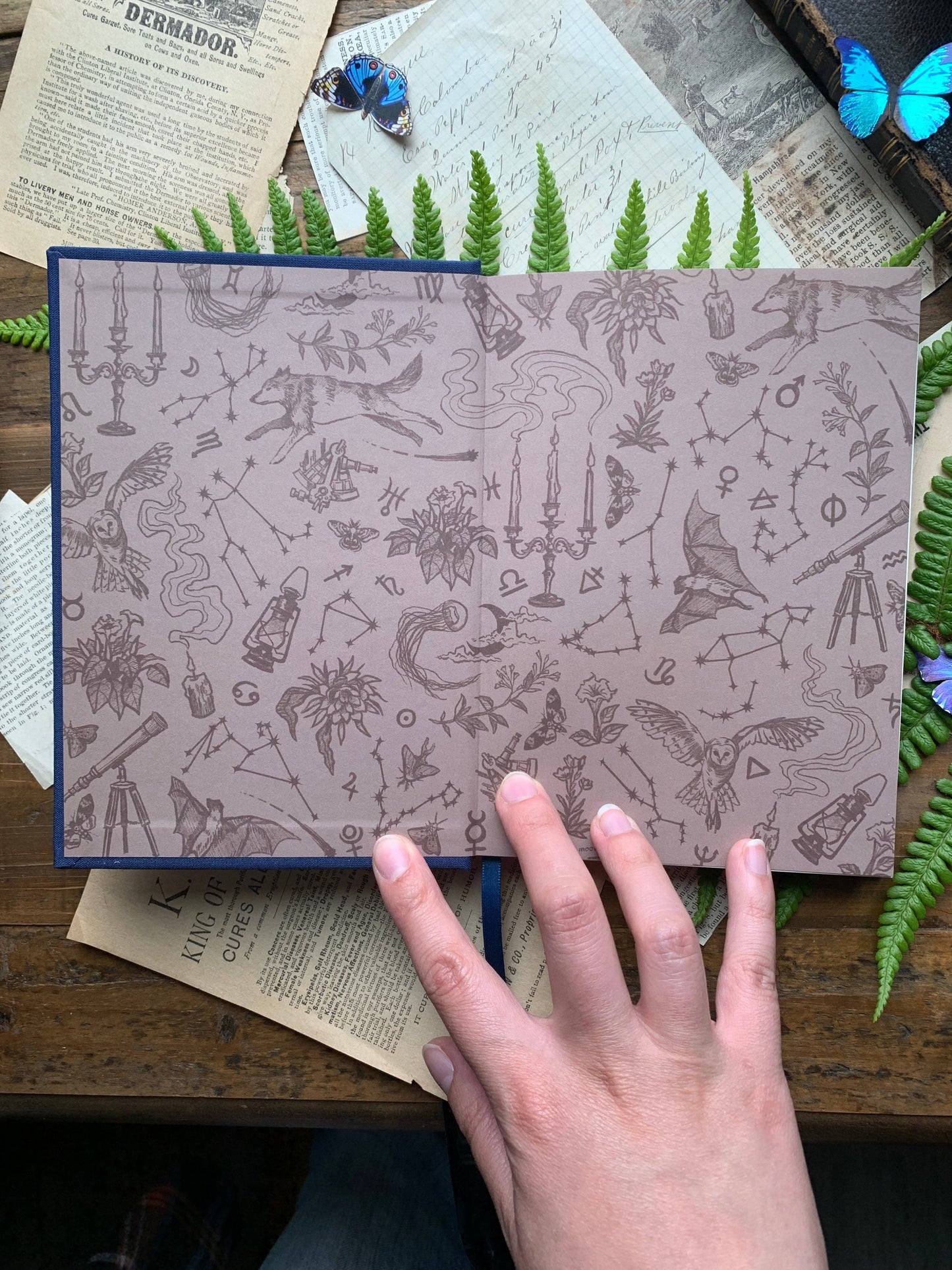 Patterned interior notebook with a hand on top, surrounded by greenery and vintage books.