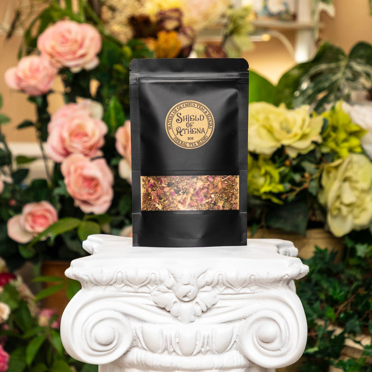 Black tea bag with a decorative label on a white pedestal in front of flowers