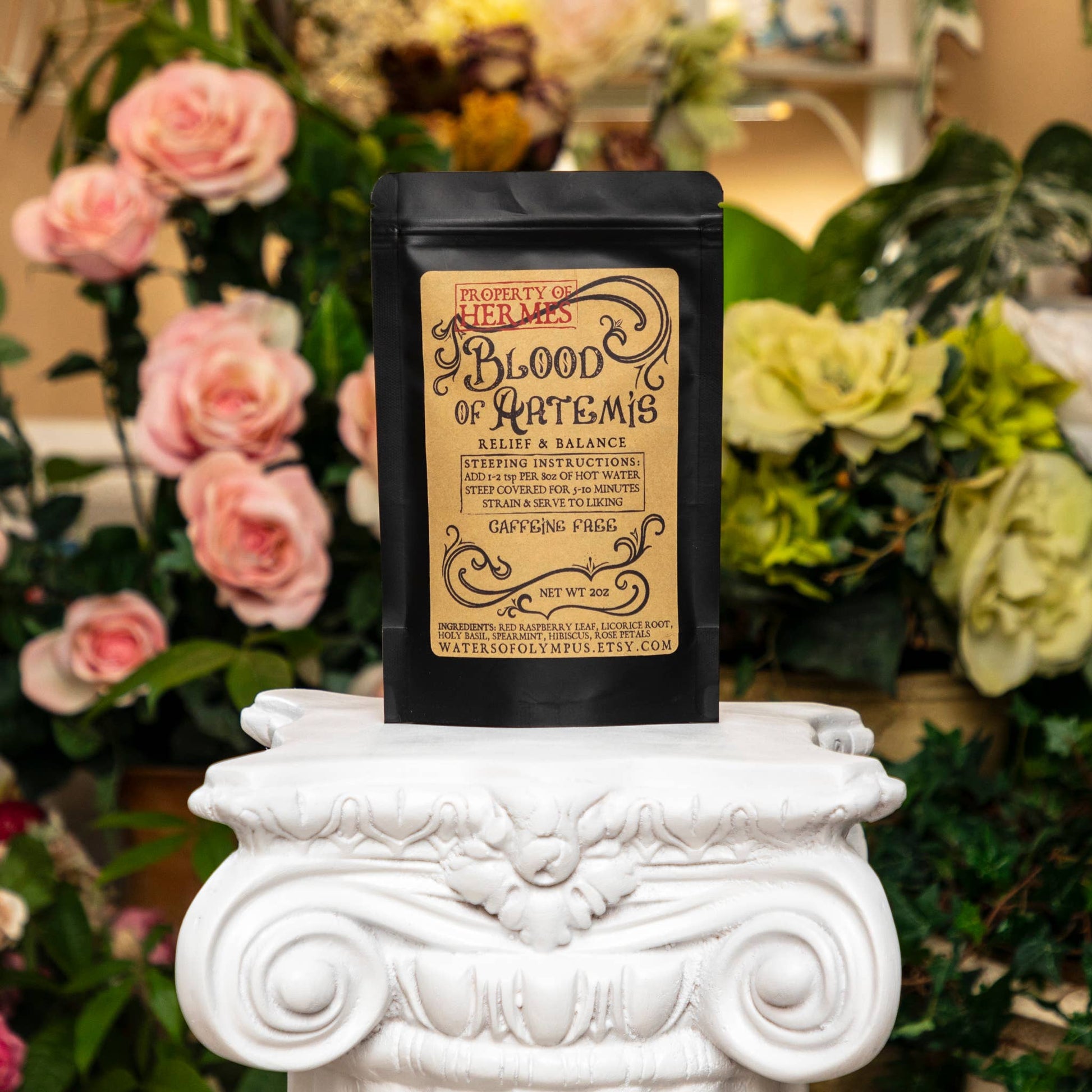 Black tea bag with decorative text on a white pedestal surrounded by flowers