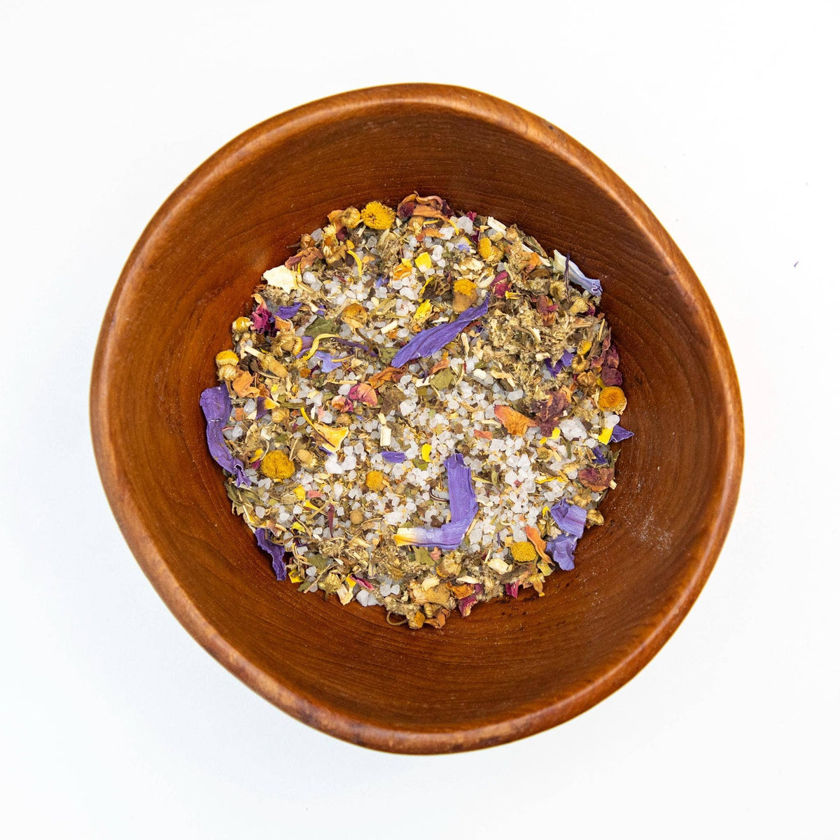 Wooden bowl filled with a mix of dried flowers and herbs on a white background