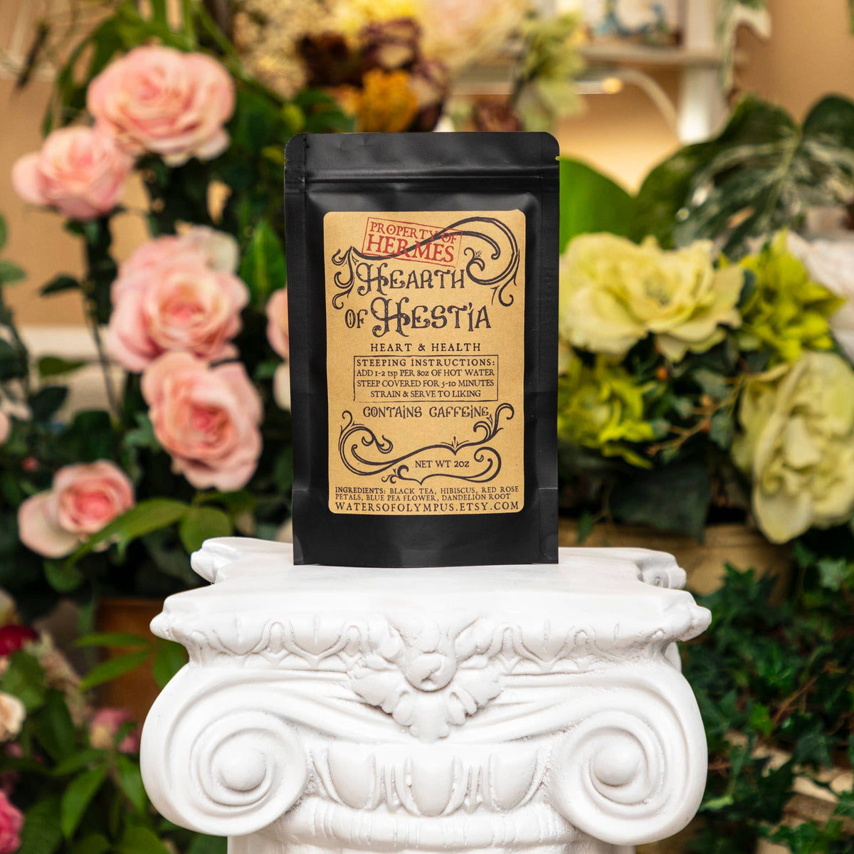 Black tea bag with decorative text on a white pedestal in front of flowers