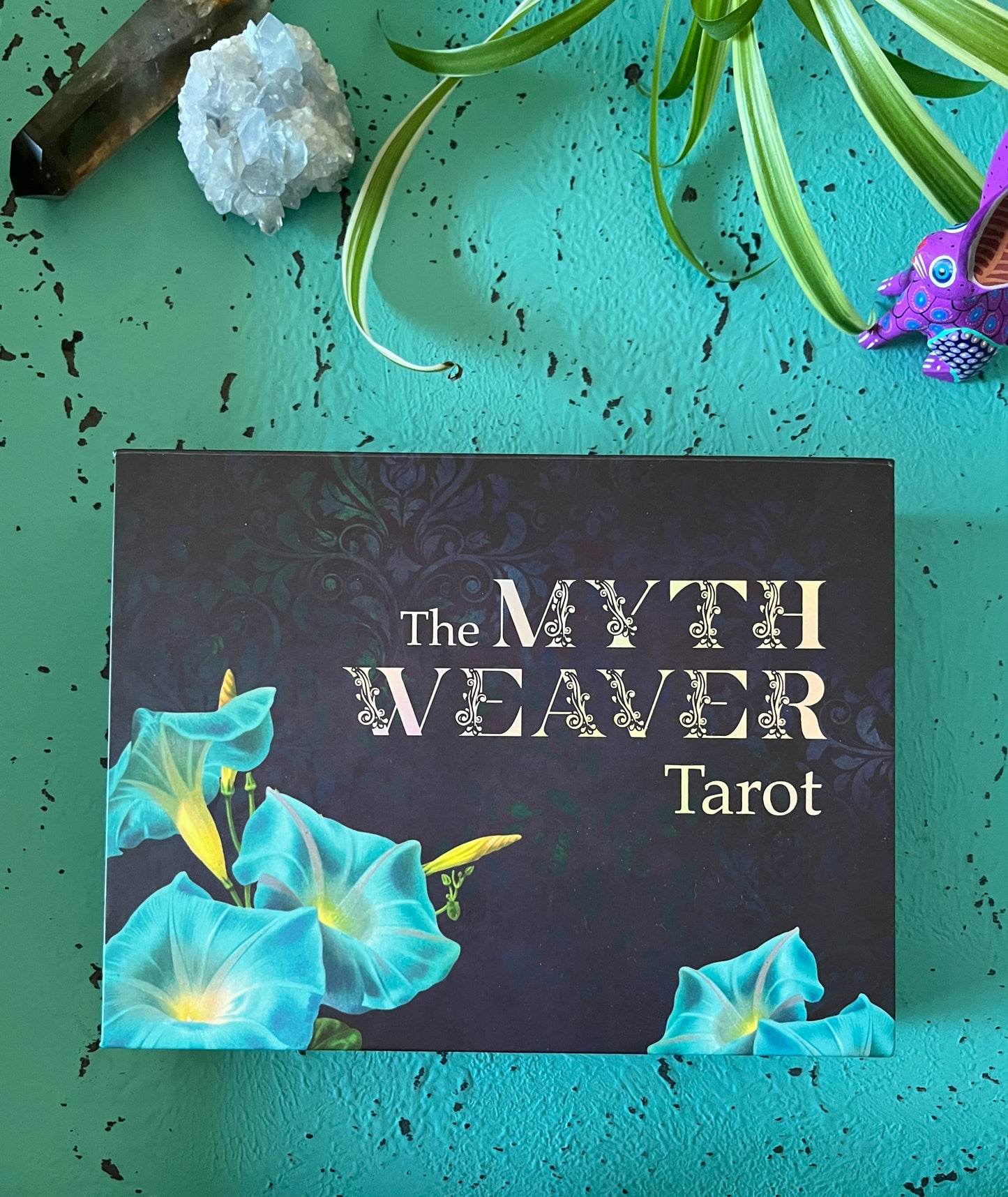 Tarot card deck titled 'The Myth Weaver Tarot' with decorative elements on a teal background.
