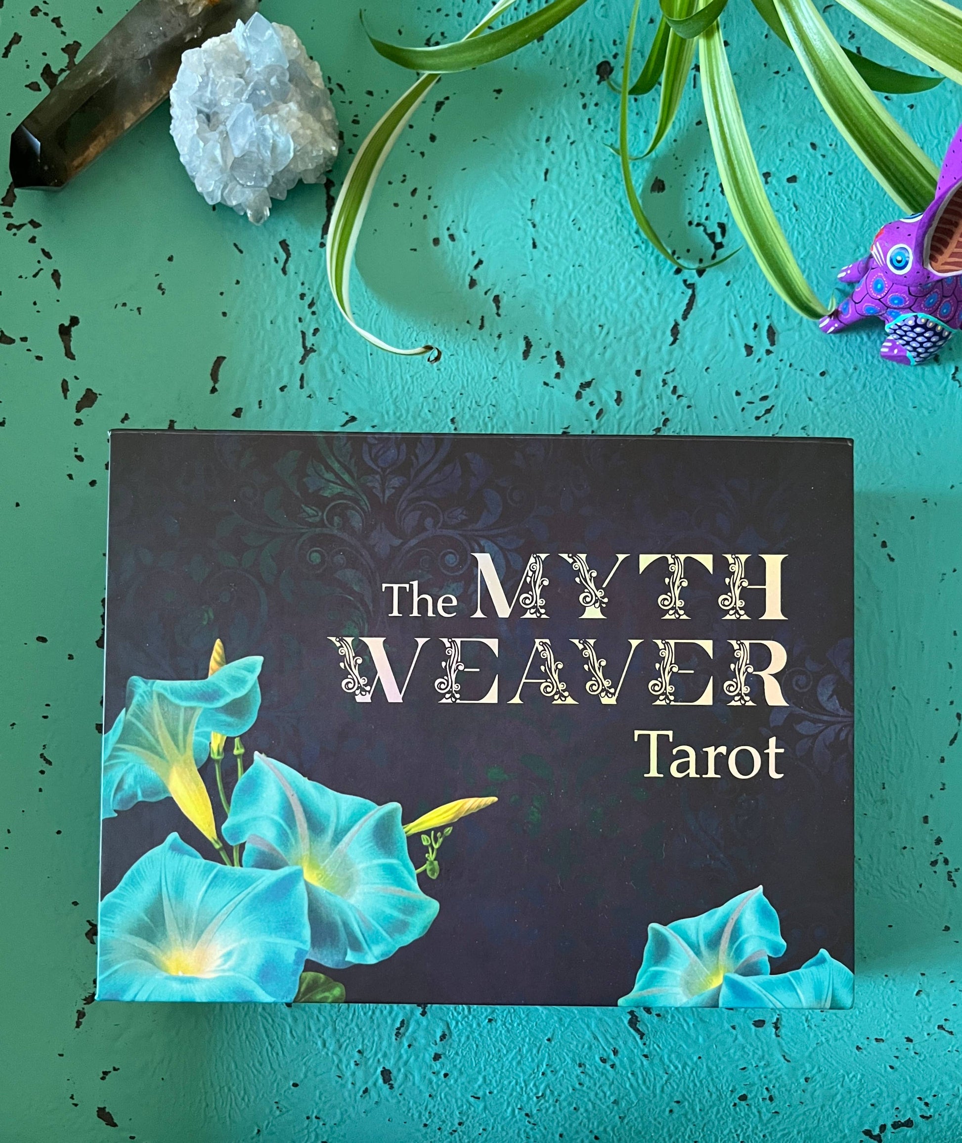 Tarot card deck titled 'The Myth Weaver Tarot' with decorative elements on a teal background.