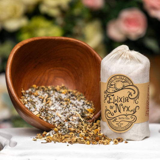 Wooden bowl with bath tea and a labeled bag of Elixir of Nyx on a blurred floral background