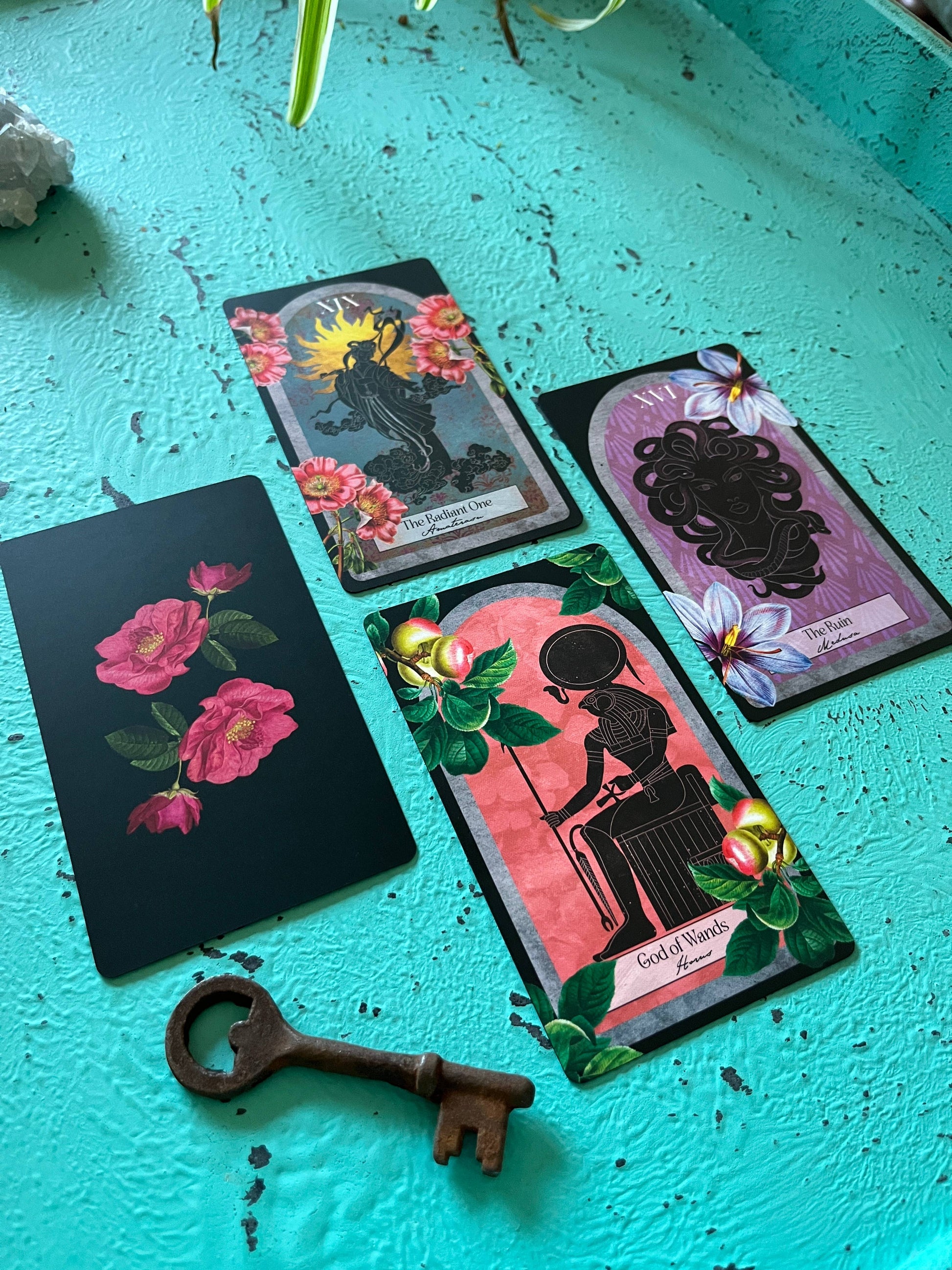 Four tarot cards with floral and silhouette designs on a turquoise surface, accompanied by a vintage key.