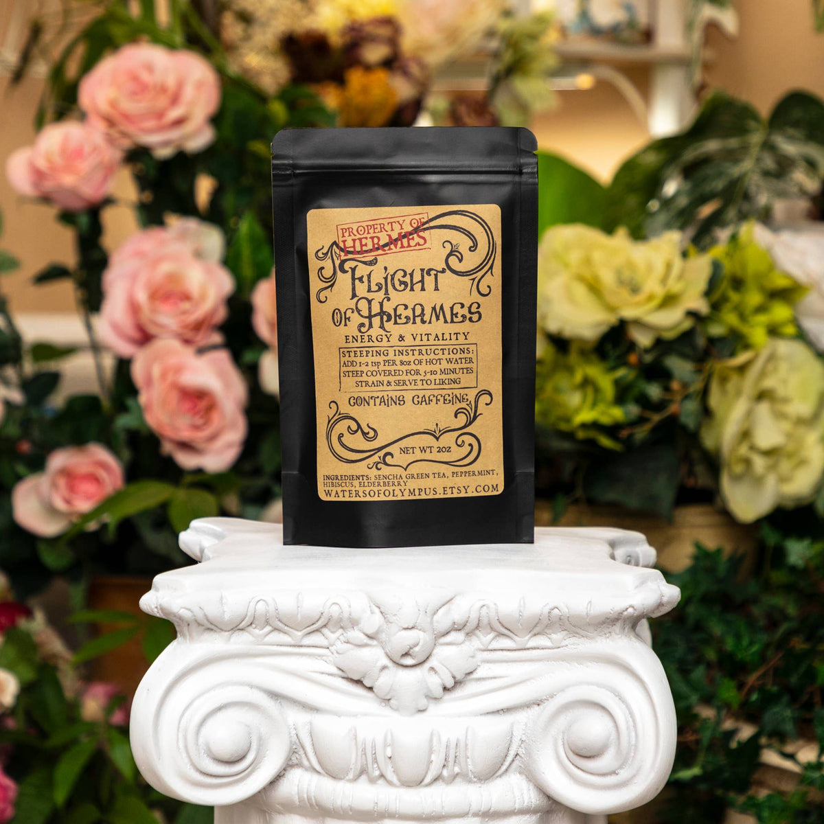 Black tea bag labeled 'Flight of Hermes' on a decorative white pedestal with flowers in the background