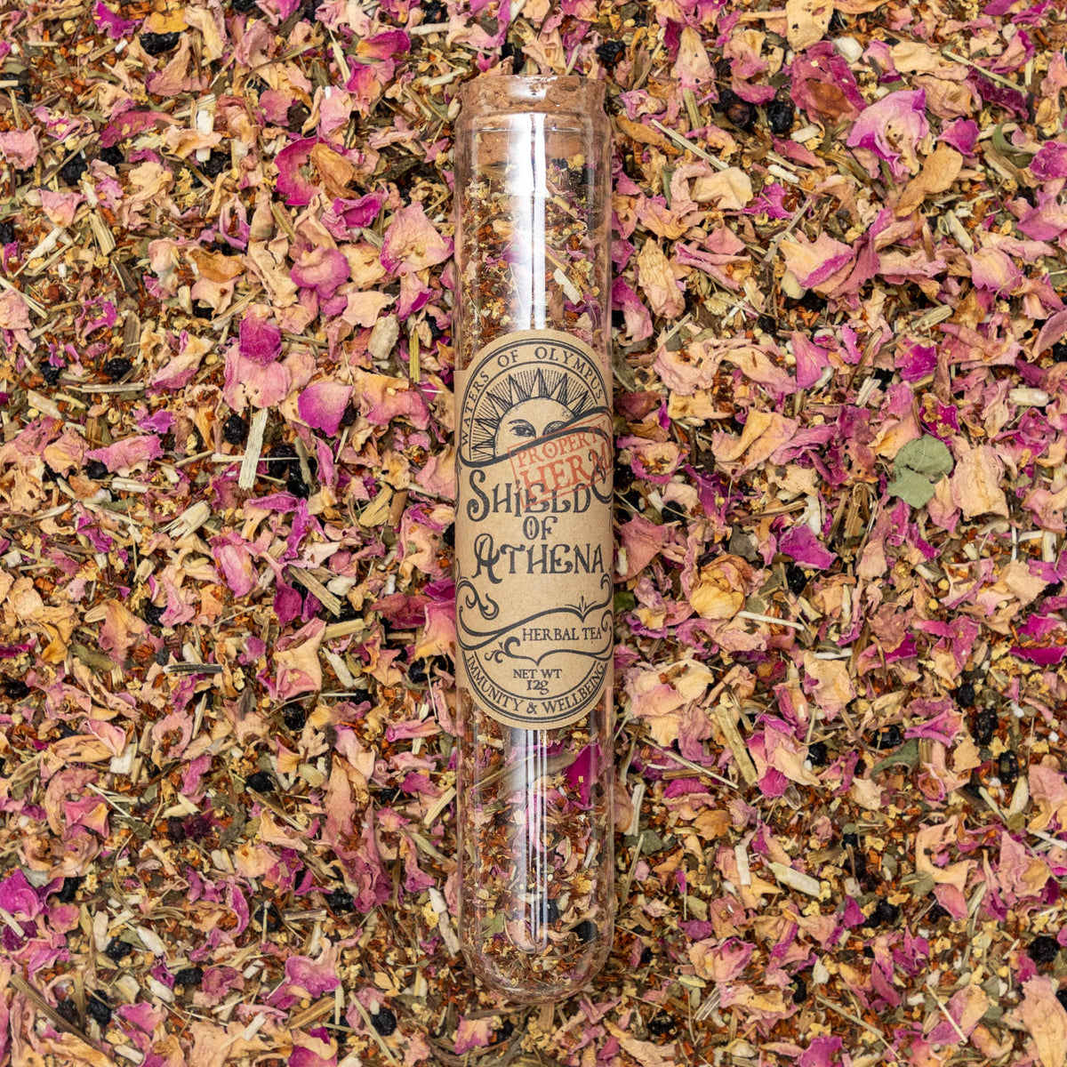 Herbal tea packaging labeled 'Shield of Athena' on a bed of dried herbs and flowers.
