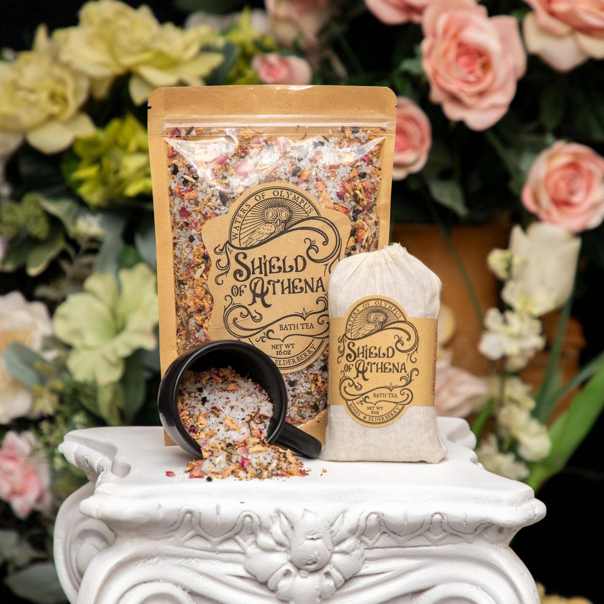 Sheath of Athena bath tea packaging with a scoop and bag on a decorative stand with flowers in the background