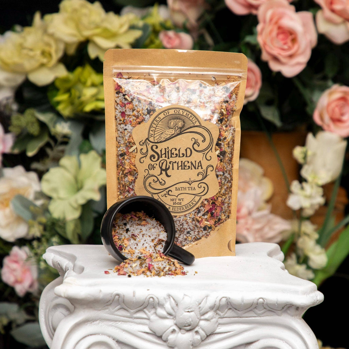 Packaged bath tea with a black mug on a white pedestal against a floral background