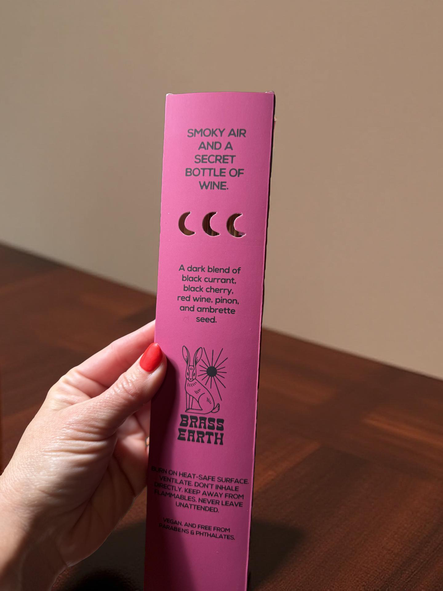 Pink product packaging held by a hand on a wooden surface