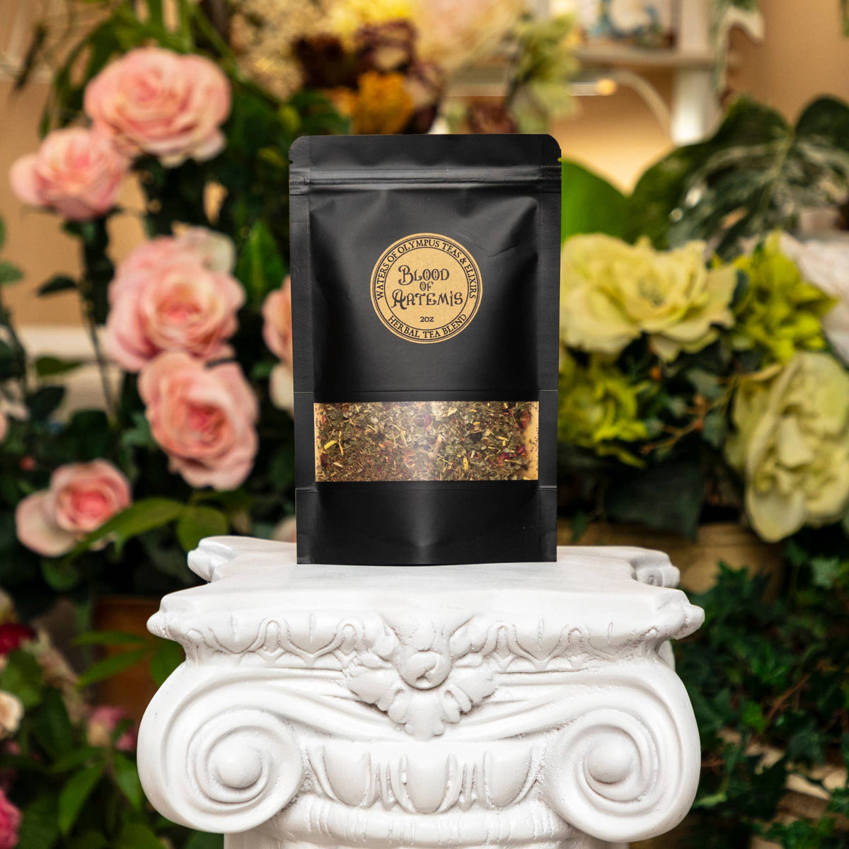 Black tea bag with visible branding on a decorative white pedestal with flowers in the background
