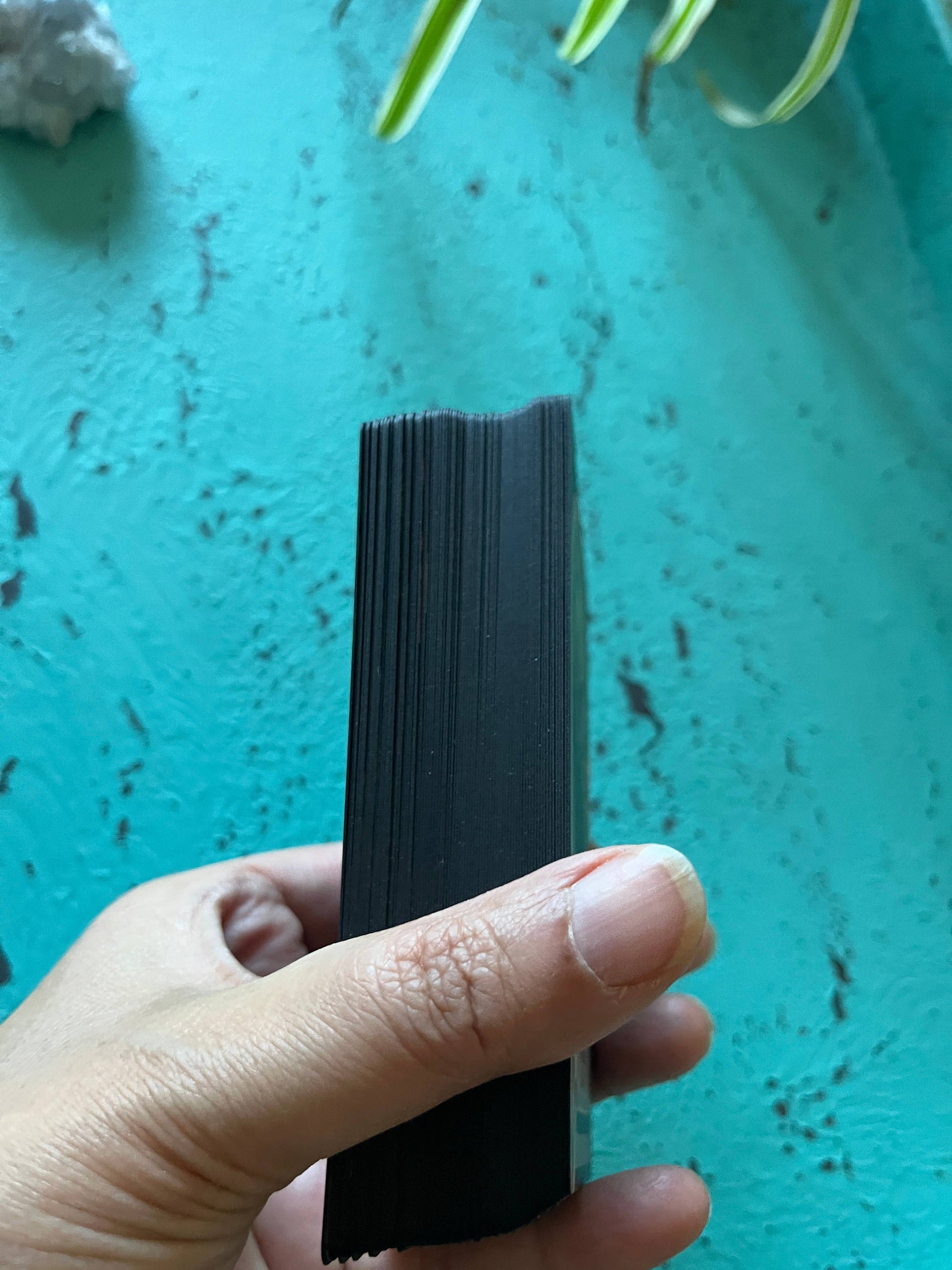 Hand holding a stack of black cards against a teal background