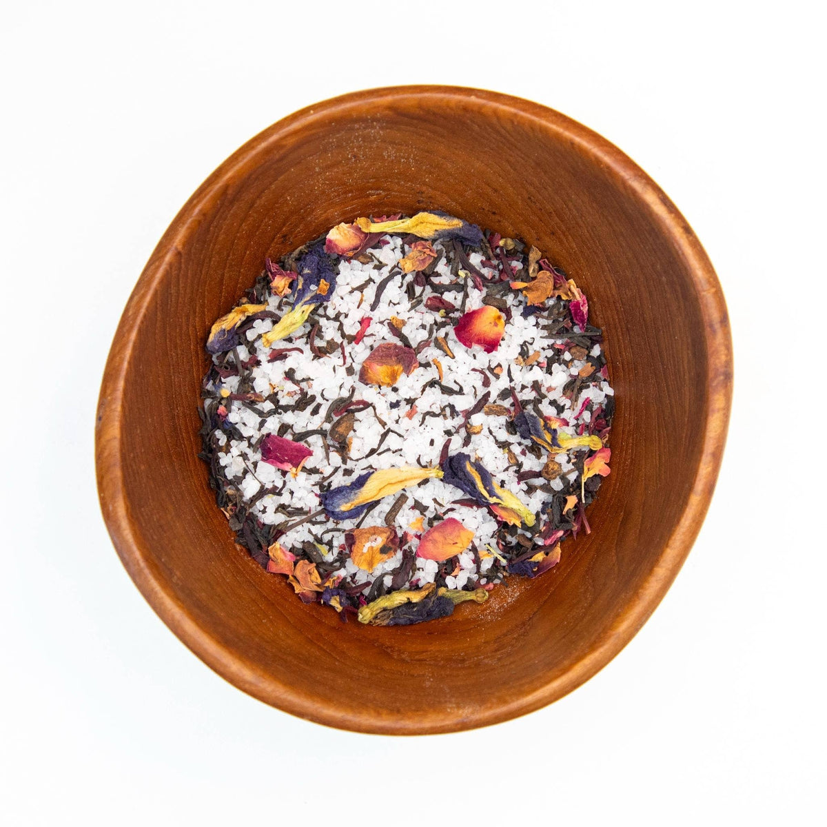 Wooden bowl filled with colorful dried tea leaves on a white background