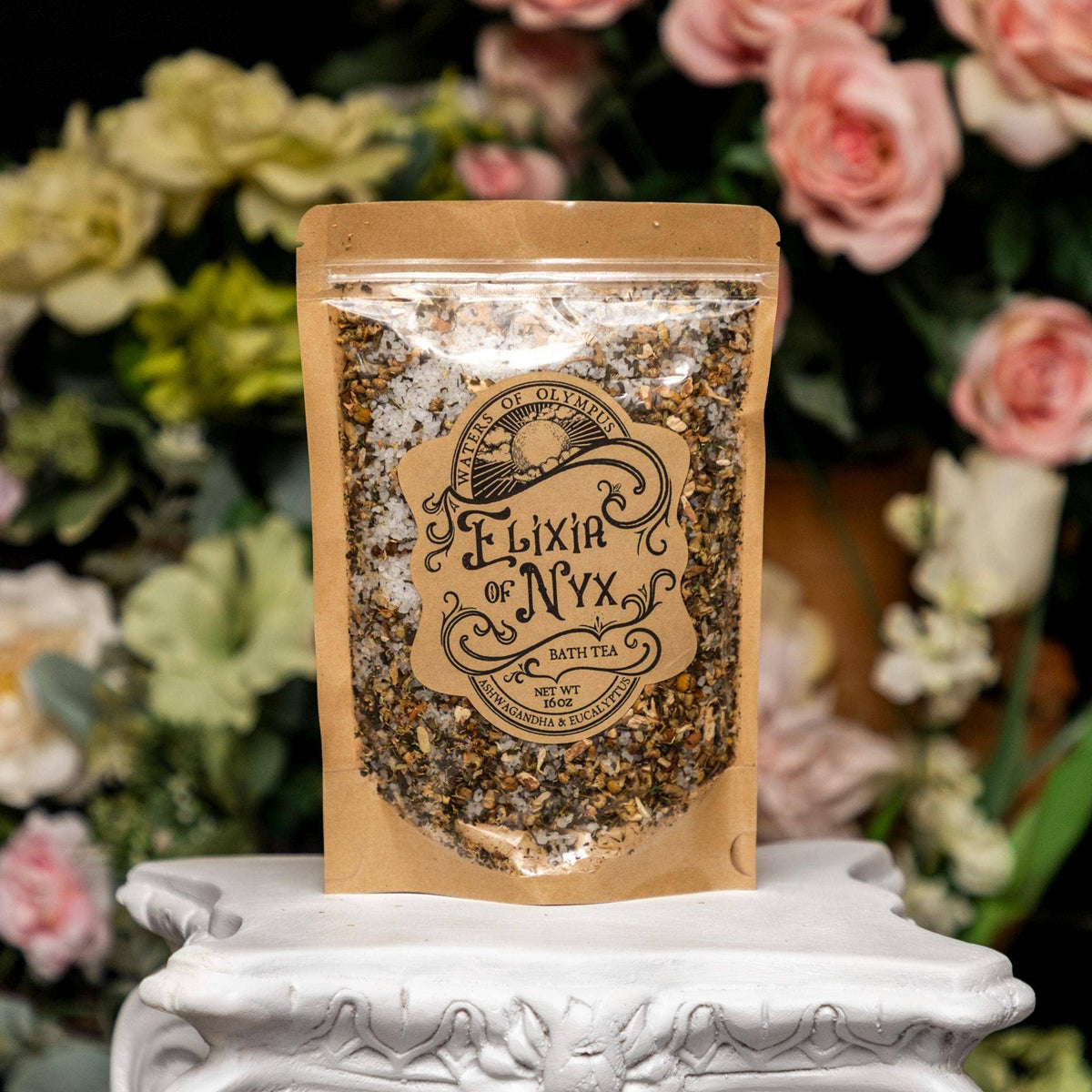 Bag of 'Elixir of Nyx' bath tea on a decorative stand with flowers in the background