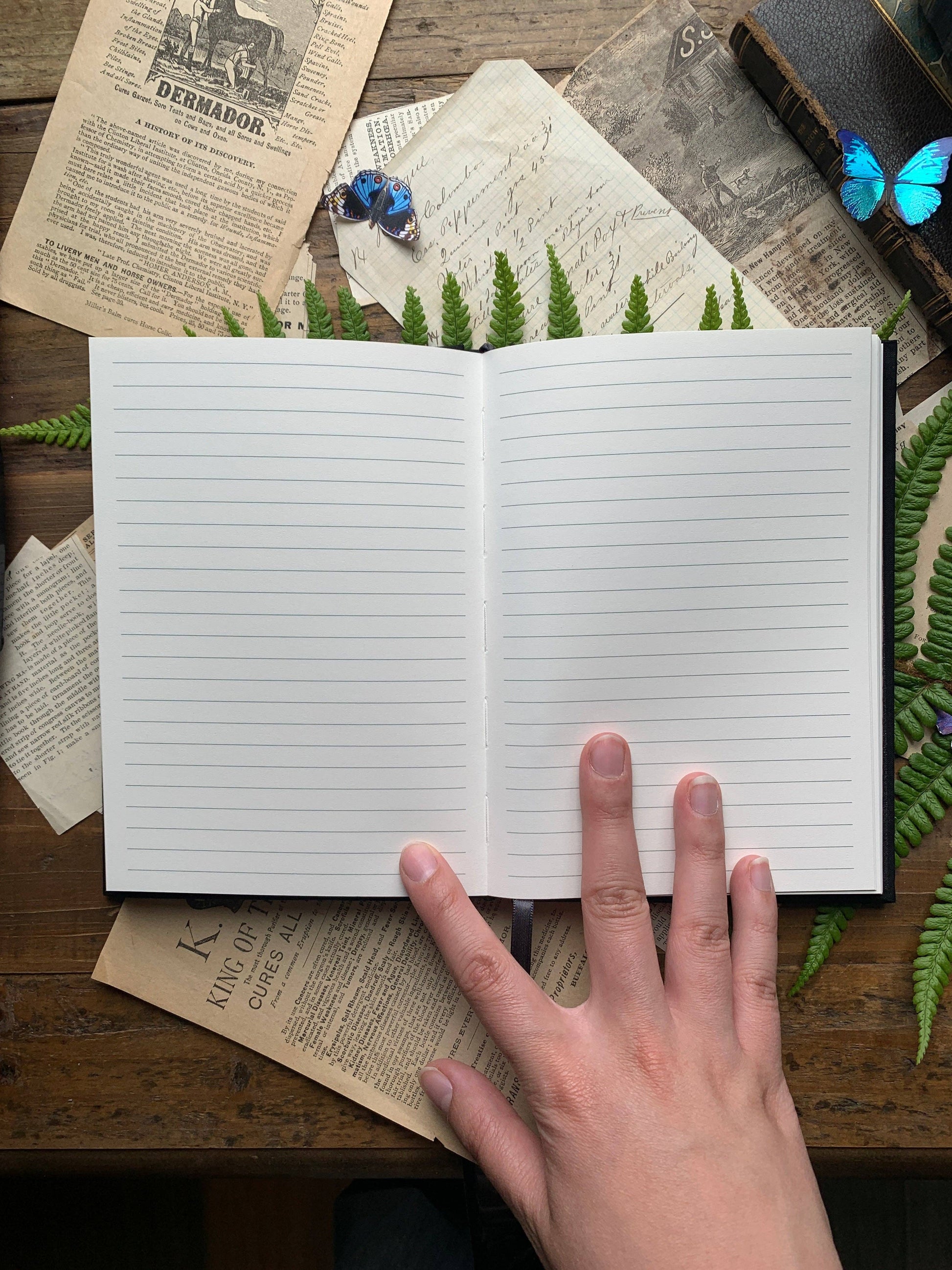 Lined interior notebook with a hand on top, surrounded by greenery and vintage books.