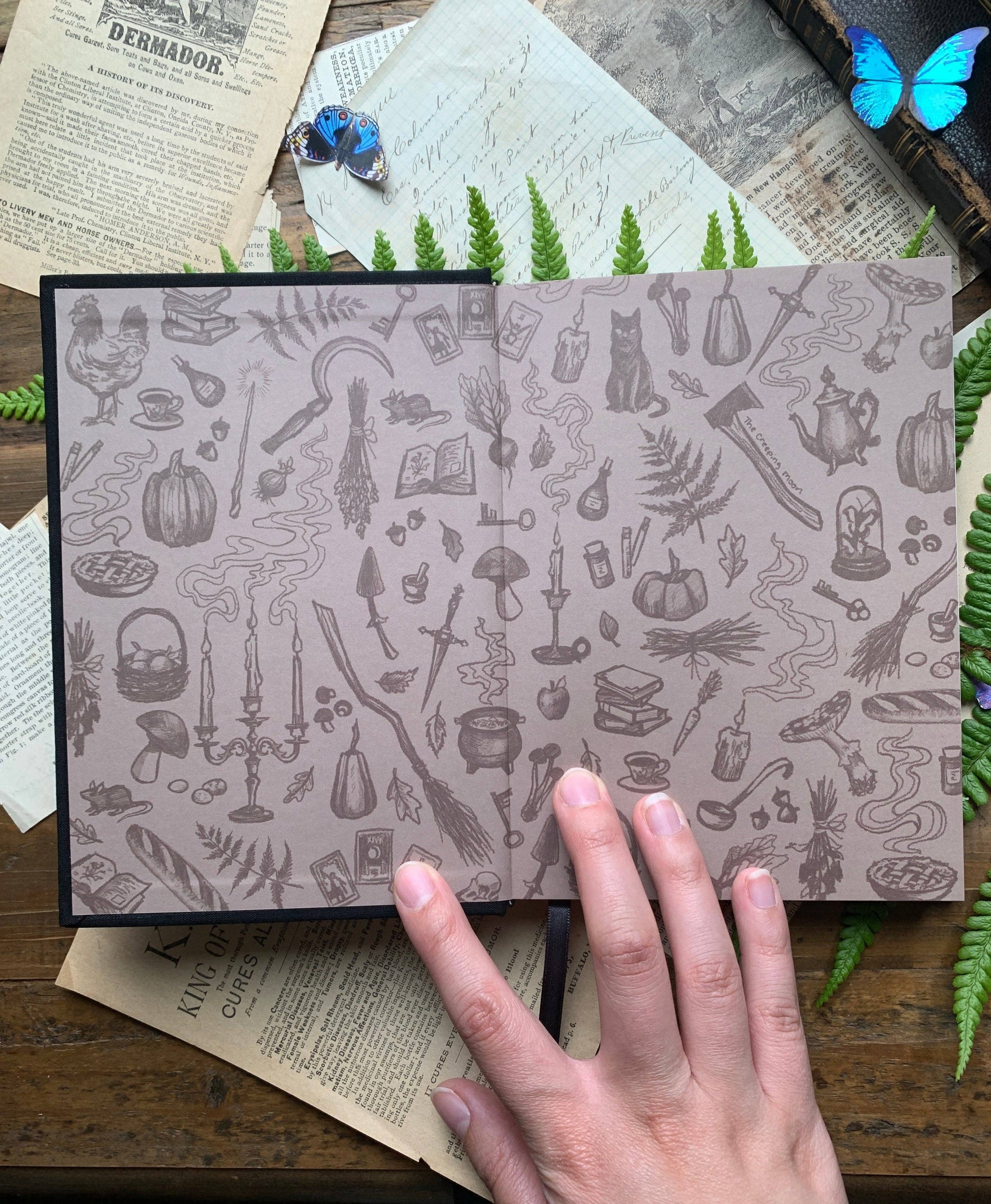 Patterned interior notebook with a hand on top, surrounded by greenery and vintage books.