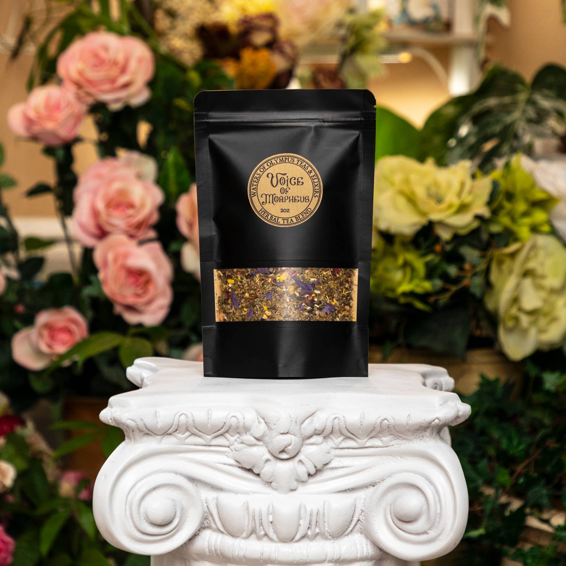Black tea packaging with gold accents on a decorative white pedestal against a floral background
