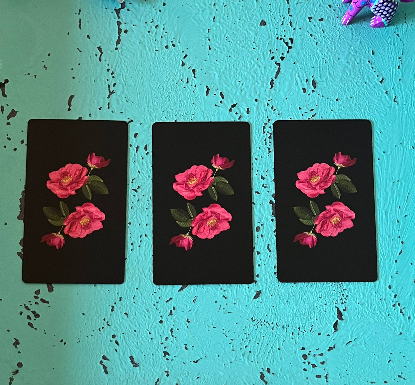 Three tarot cards with pink flower designs on a textured teal background