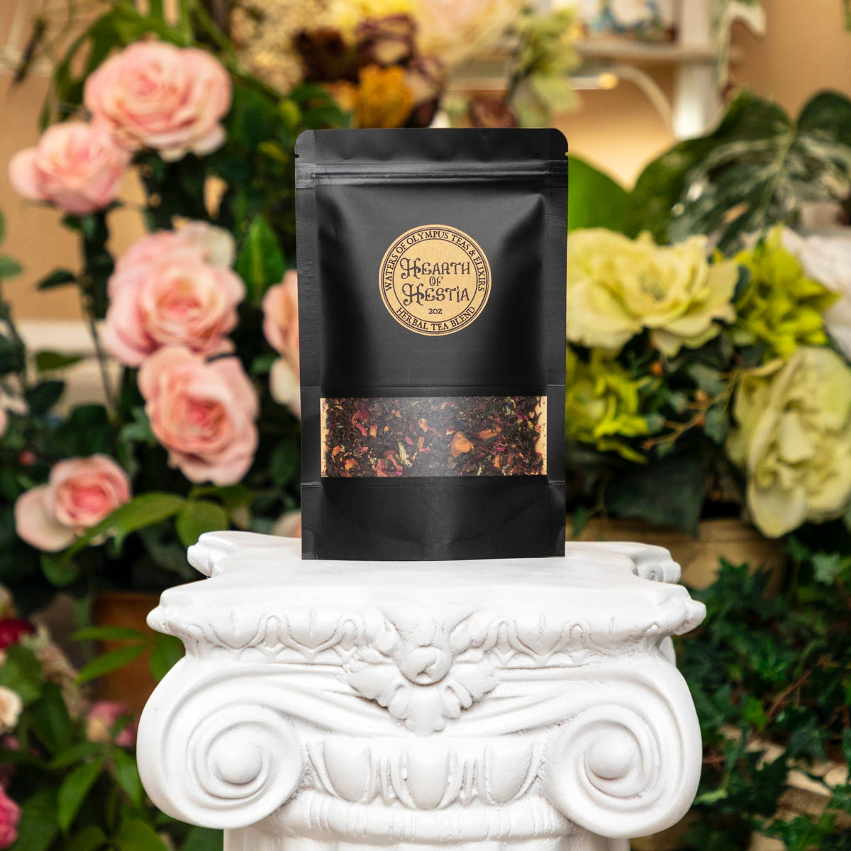 Black tea bag with visible brand logo on a decorative white pedestal with flowers in the background