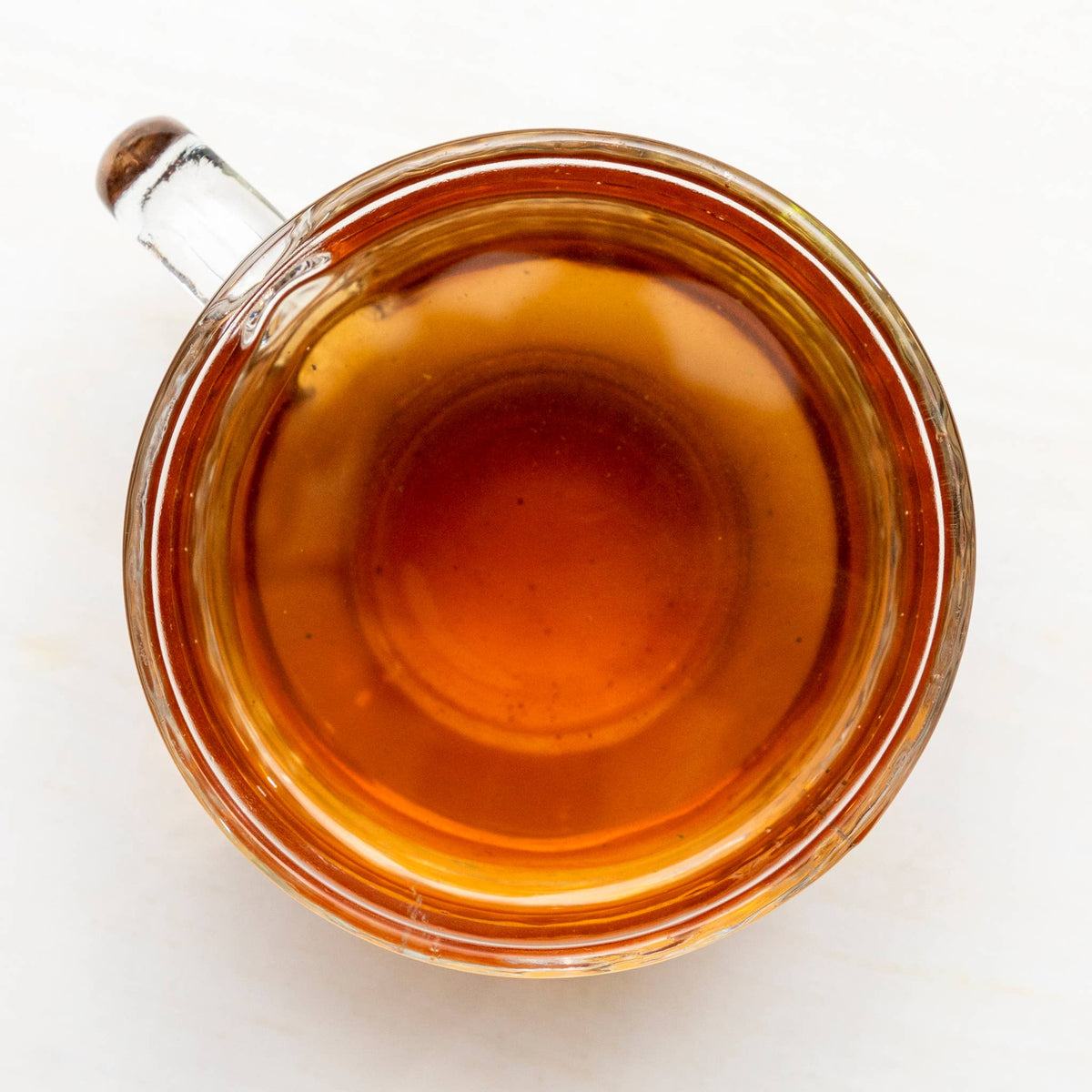 Clear glass mug filled with a warm brown tea on a white background