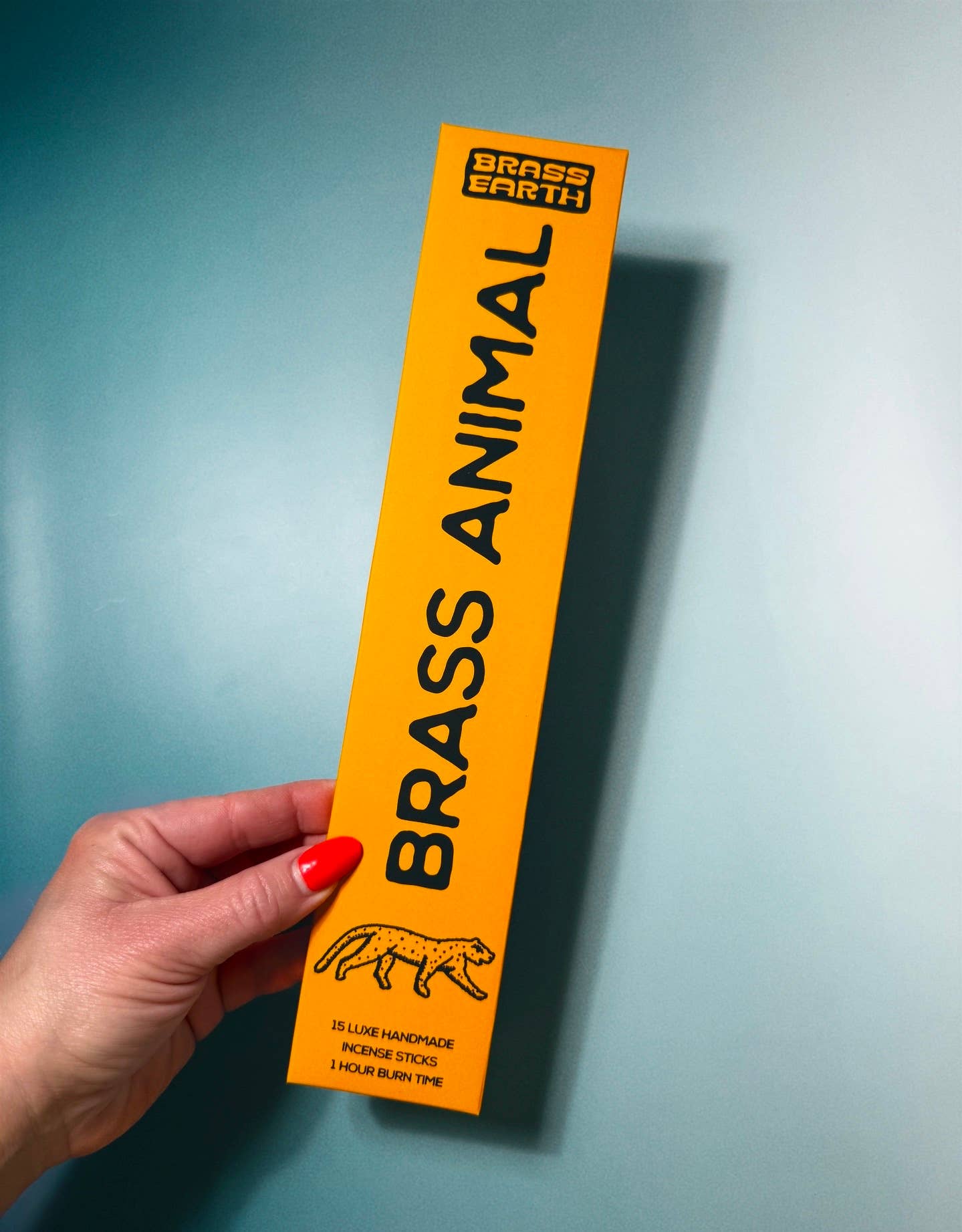 Hand holding a yellow 'Brass Animal' product packaging against a blue background