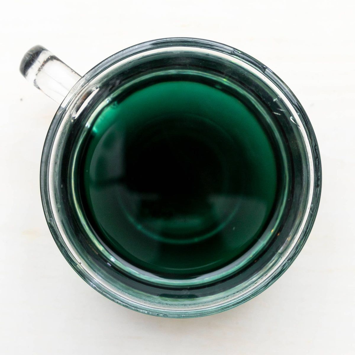 Clear glass mug filled with dark green tea on a white background