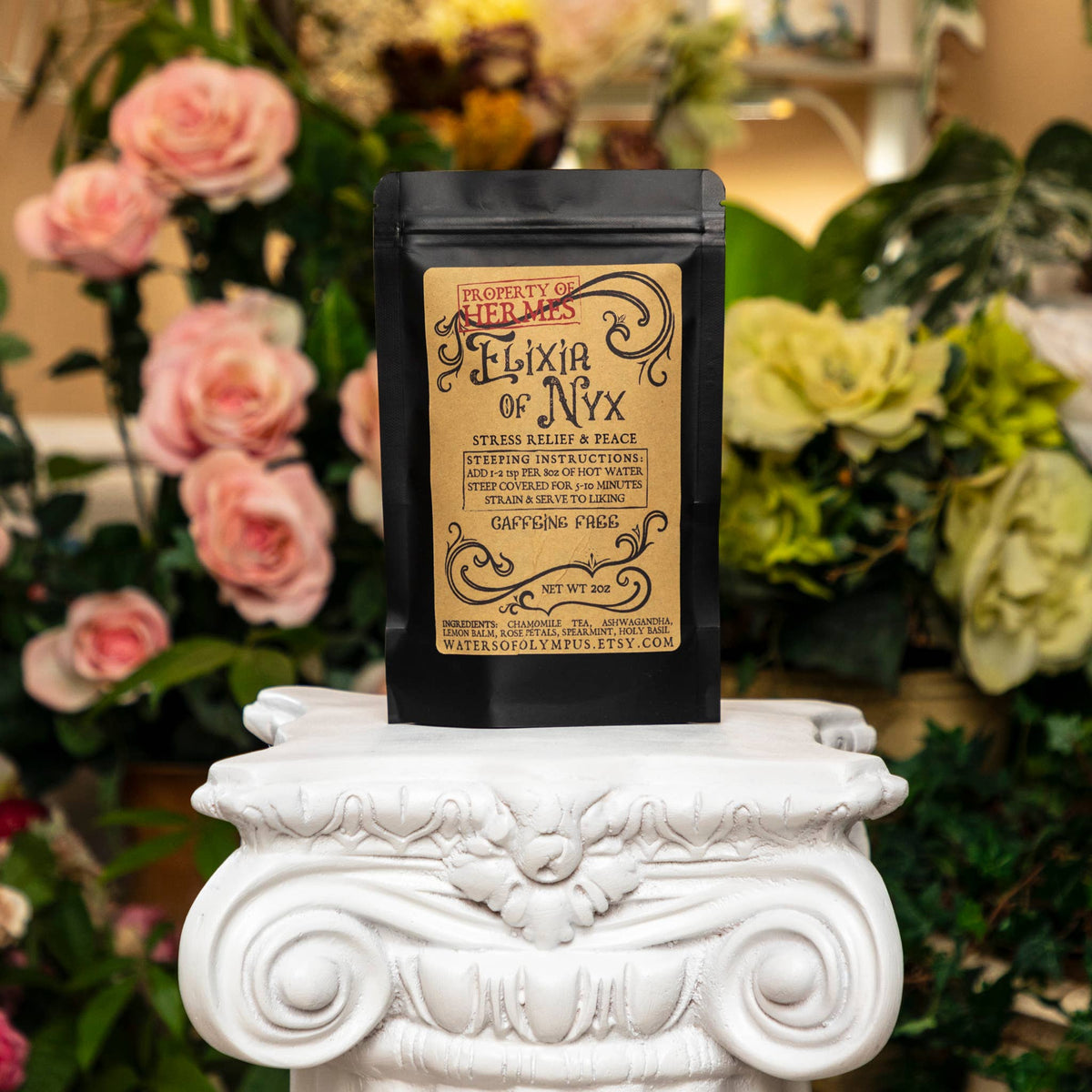 Black package labeled 'Elixiar of Nyx' on a decorative white pedestal with flowers in the background