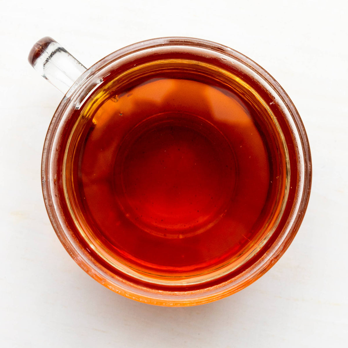 Clear glass mug filled with red tea on a white background