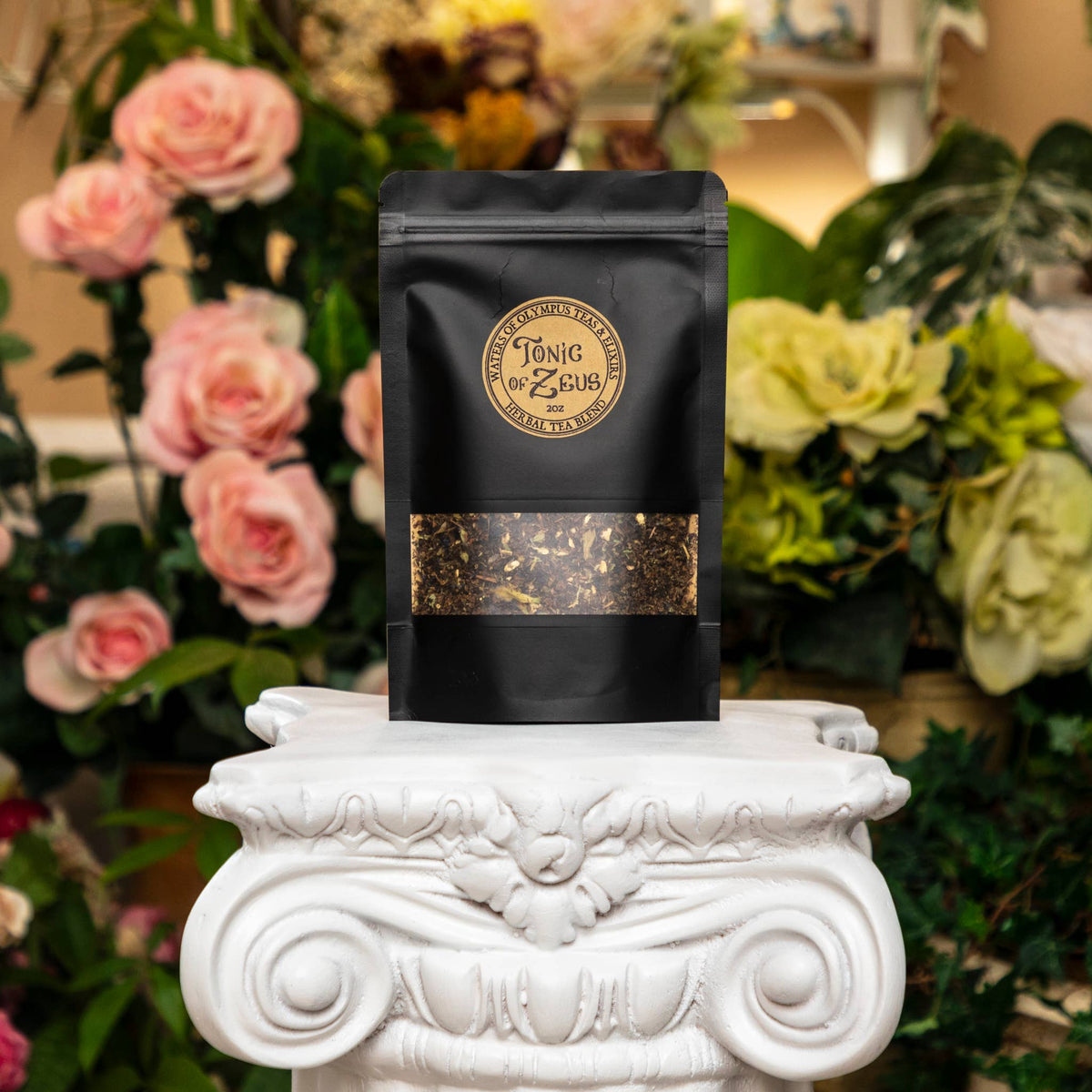 Black tea bag with 'Tonic Zeus' branding on a decorative white pedestal with flowers in the background