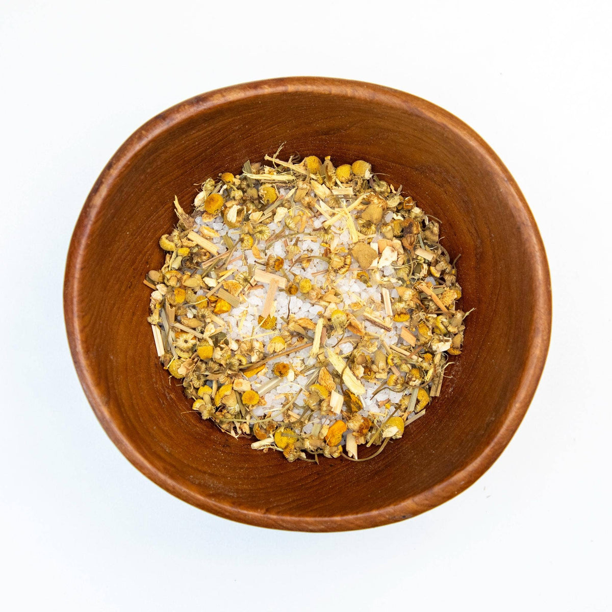Wooden bowl filled with dried herbs and salts on a white background
