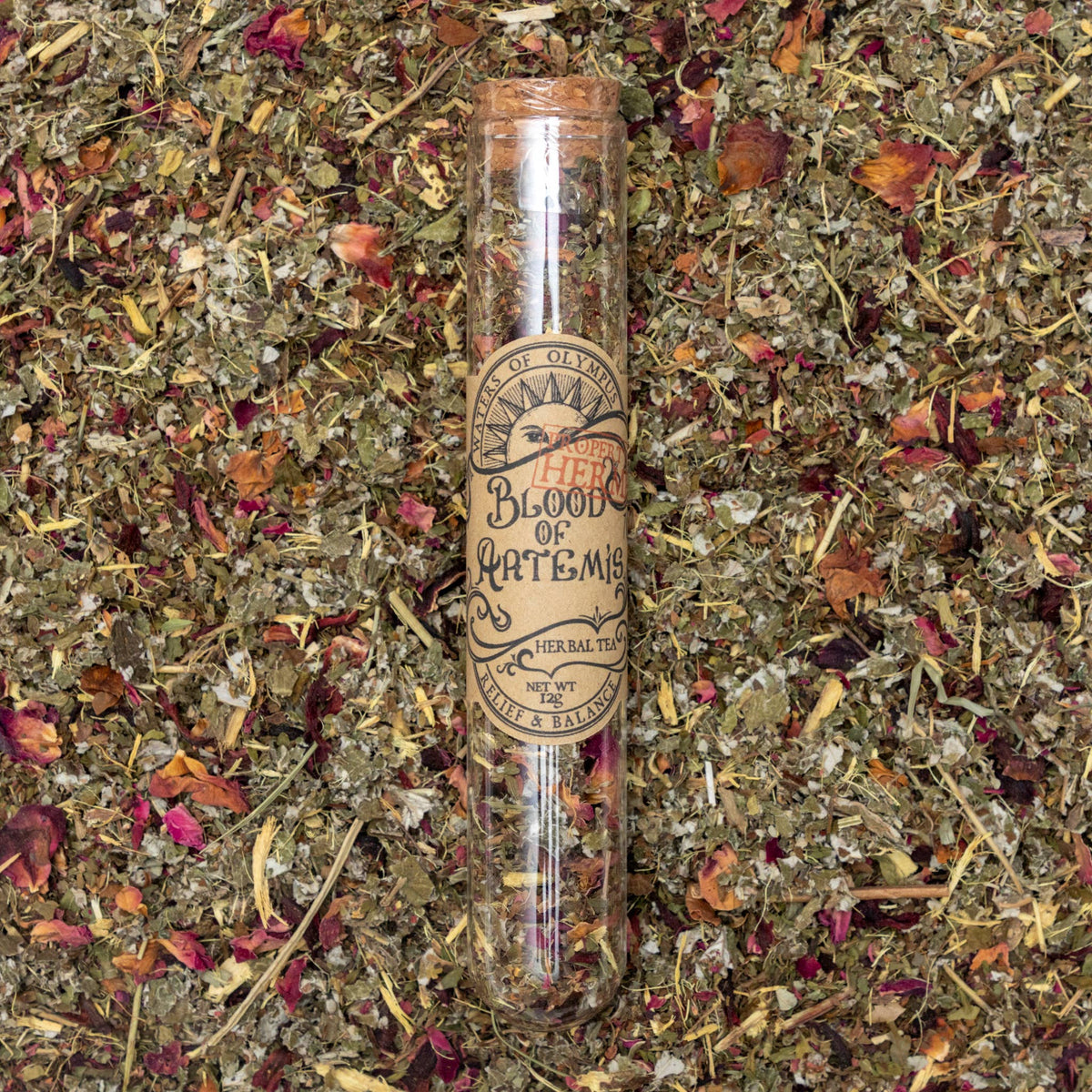 Herbal tea packaging labeled 'Blood of Artemis' on a bed of dried herbs and flowers.