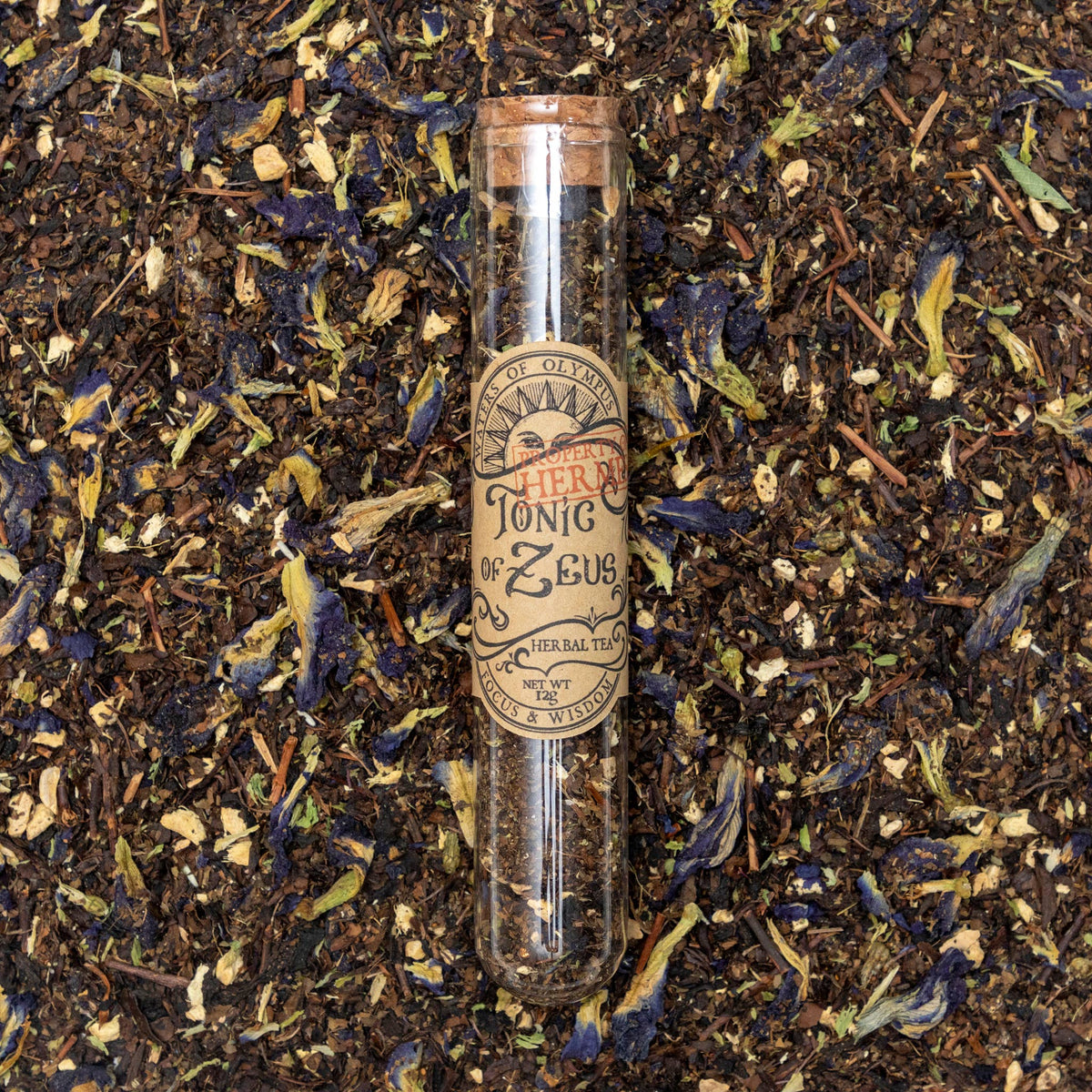 Herbal tea packaging labeled 'Tonic of Zeus' on a bed of dry tea leaves.