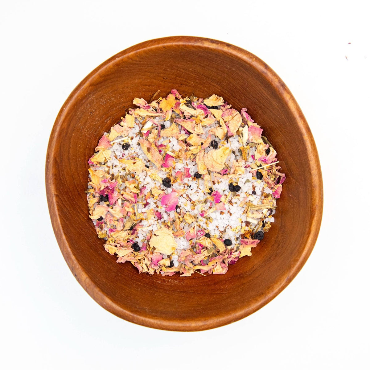 Wooden bowl filled with a colorful mix of dried flowers and herbs on a white background