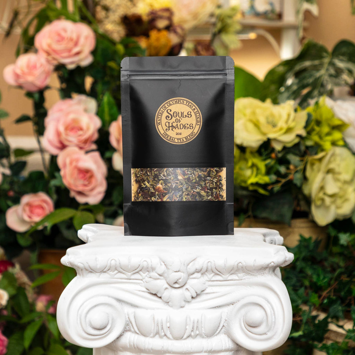 Black tea bag with a label on a decorative white pedestal in front of flowers