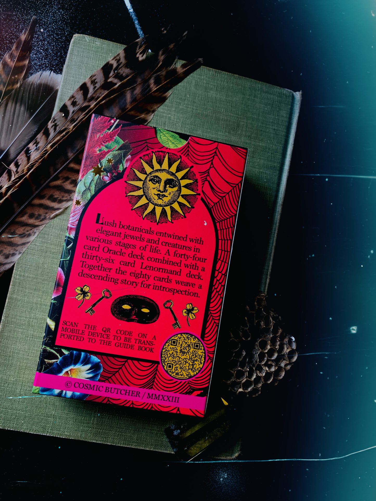 Packaging of 'Cosmic Bureaucrat's Walk Through the Eternal Gardens' Oracle and Lenormand cards on a book. Back of box features sun design and text 